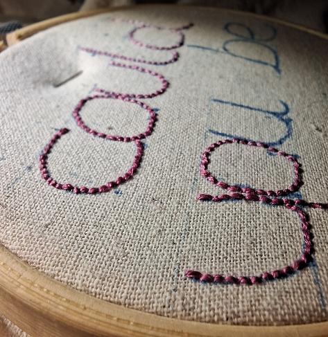 Photo très rapprochée d'un tissus tendu sur un tambour de broderie. Il est brodé "could you be" en rose