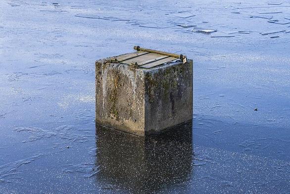 View of the frozen Knollenteich in Hof (Saale), Bavaria, Germany. The cube-shaped concrete water drainage system is completely surrounded by the frozen pond.