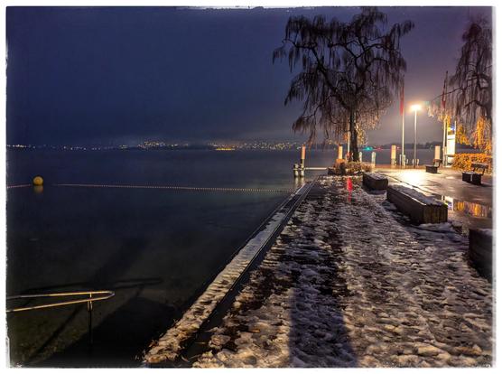 A pier at night. Some snow on the ground, otherwise wet and dark.