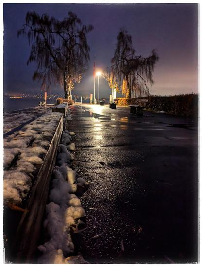 .A path leading to a boarding ace for ships. It is dark, street lamps give some light. It is wet, some rest of snow.