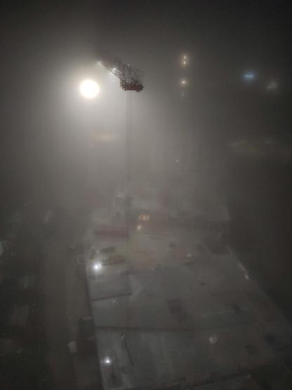 un chantier de nuit dans le brouillard en haut une lumière et une flèche de grue qui semble apparaitre de nulle part