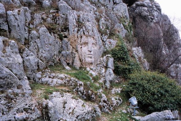 Farbfoto einer Felslandschaft mit etwas Grün dazwischen. In Bildmitte ein in den Felsen gehauenes Gesicht im Stil einer klassischen römischen Skulptur. Leica R3 auf Agfa Precisa-Film.