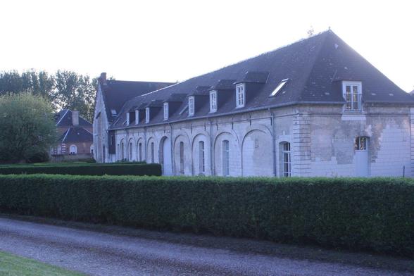 Abbaye de Blangy. 
Une coursive en pierre blanche, avec des toits en tuiles.
Au premier plan une haie taillée très carrée.