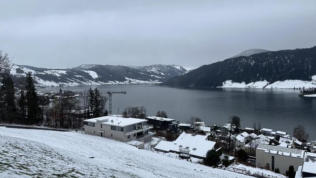 View past snowy fields to lake Ägeri on a gray rainy day under an overcast sky.