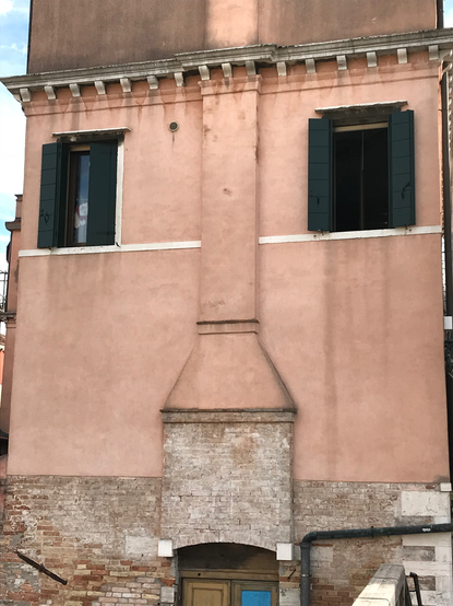 Fassade eines schmalen Hauses in Venedig - zwei Fenster oben wirken wie Augen neben einem gemauerten Kamin, der wie eine Nase aussieht.
Der umlaufende Sims über den Fenster kann als Haar durchgehen.
Unten ein leicht runder Türsturz über der Eingangstür, der wie der Mund dazu passt.