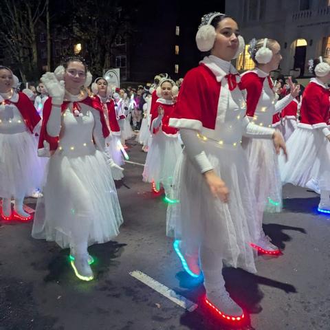 Group of performers in red capes and LED-lit shoes waving during nighttime parade.