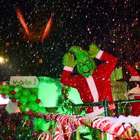 Grinch character on decorated float with Whoville sign, candy canes, and fireworks overhead.