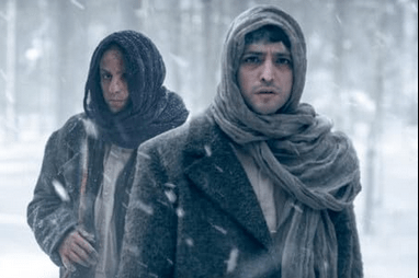 Ihsan (played by Erkan Kolçak Köstendil) and Ziya (played by Taner Ölmez) standing in the snow. Ihsan is behind Ziya. Both men are swathed in the same clothes - a headscarf and heavy coat - and mirror each other. Ihsan is the Creature here, and his headscarf is black. Ziya's is a lighter grey.