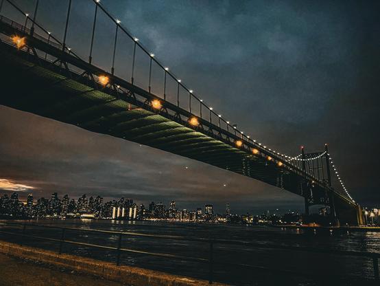 Nighttime in Astoria Park overlooking the RFK Bridge. Lights from the bridge and buildings reflect on the river.