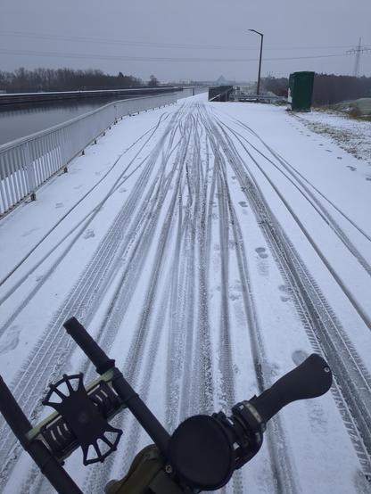 über den Fahrradlenker hinweg fotografierter Weg mit vielen Fahrradspuren im Schnee