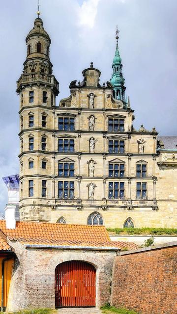 A vertical image capturing the Renaissance facade and towers of Kronborg Castle in Helsingør, Denmark, viewed over a brick archway.