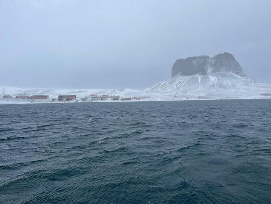 Ein Berggipfel ist am Meer zu sehen, daneben eine Forschungsstation.