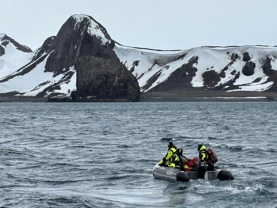 Ein Schlauchboot fährt durch eine Bucht. Im Hintergrund ein schneebedeckter Berggipfel.