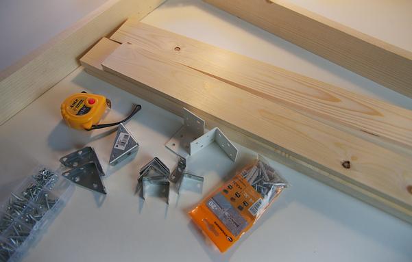 Foto de unas tablas de pino cortadas a medida junto a un puñado de tornillos y herrajes.