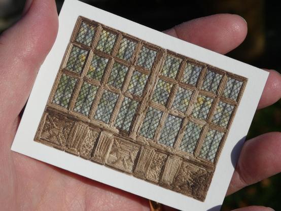 Miniature, playing card sized, print taken from a stitched artwork depicting a large, 24 panwd, stone mullioned window with leaded lights. The view through the window is green trees. Held in the artist's hand for scale