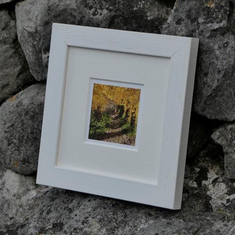 Framed miniature print taken from a stitched artwork depicting a path through autumnal woodland. Sitting against a stone wall