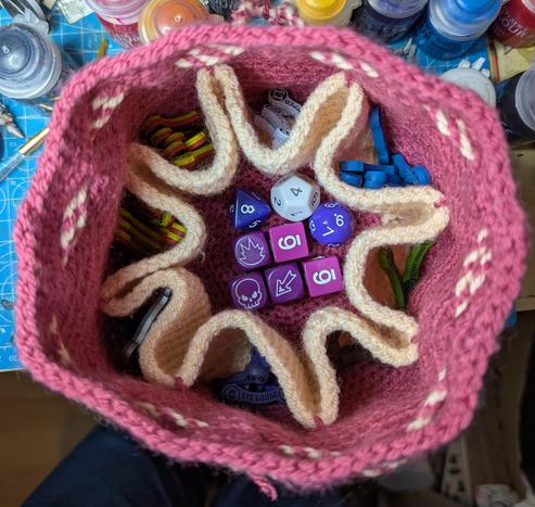 The inside of the bag seen from above, showing eight cream-coloured pockets around the edges. The central space holds various dice, while the pockets have tokens in various colours