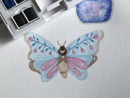 Un papillon bleu et rose à l'aquarelle et aux crayons de couleurs, avec des motifs de fleurs, lunes et étoiles.