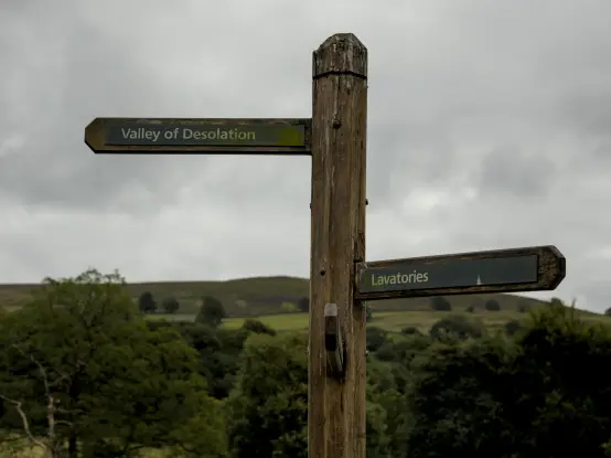 A photo of a signpost. One direction is labelled "Valley of Desolation", the other is labelled "Lavatories".