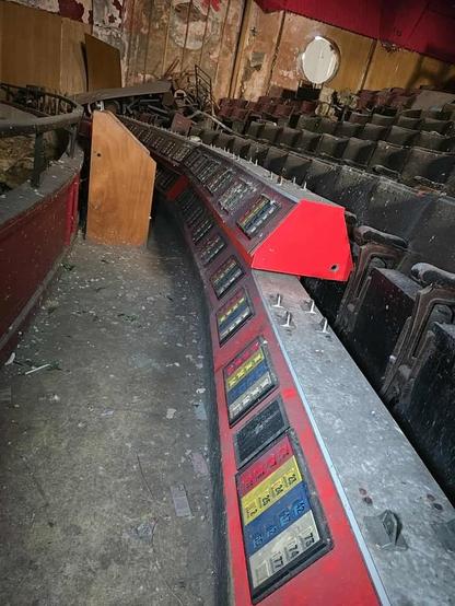 Abandoned control panel with coloured buttons in deteriorated auditorium with dusty seating and peeling walls.