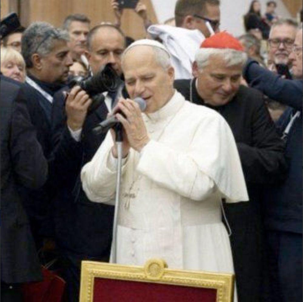Pope Leo in front of a mic stand, holding the mic and leaning in as if crooning soulfully.