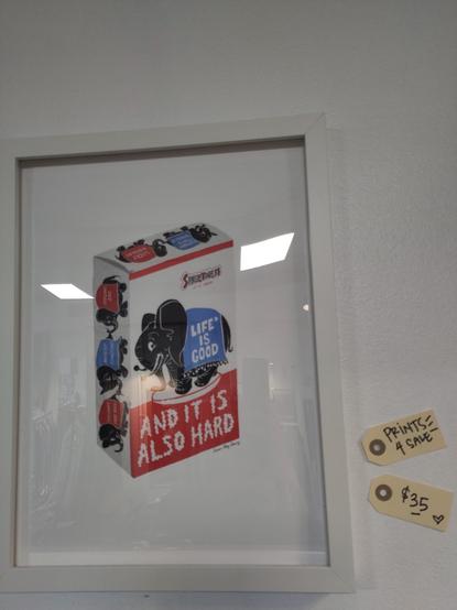a ftamed print of a piece of Artwork by Anna May Henry that looks like a box of candy popcorn, the elephant's blanket reads Life is good, and below AND IT IS ALSO HARD

labels beside say Prints for Sale $35