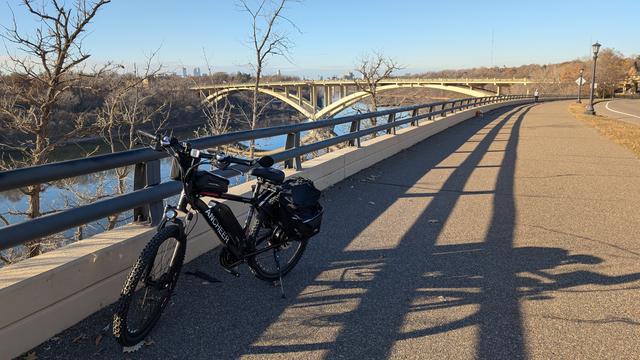 Black and red eBike in front of the Mississippi River, with the Mississippi River Bridge in the background