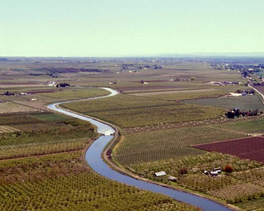 An irrigation canal flows through a valley filled with orchards.