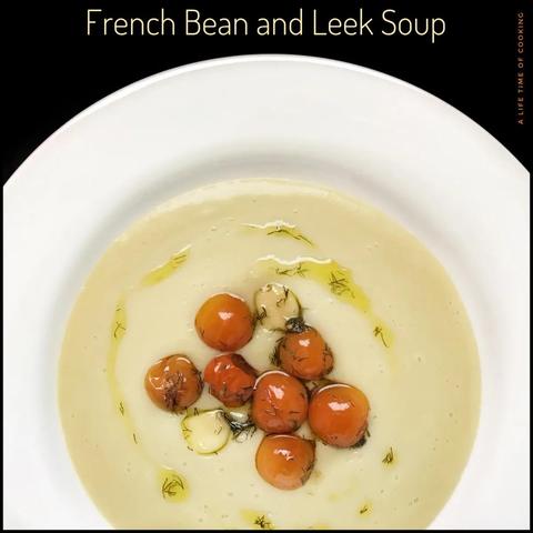 A white bowl of a creamy bean and leek soup is topped with roasted red cherry tomatoes.