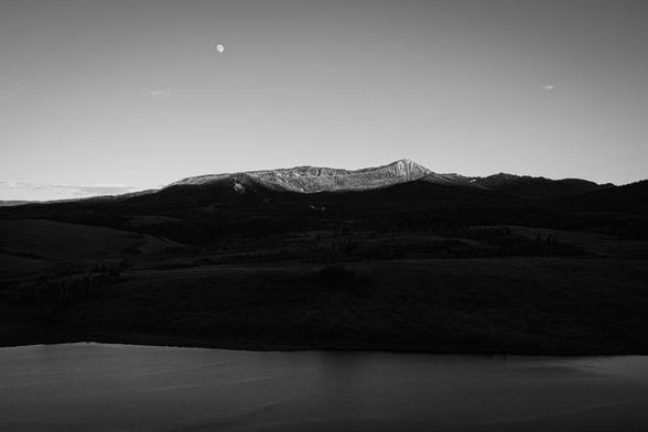 Mount Leidy at sunset, with the moon rising in the sky and the Elk Ranch Reservoir in the foreground.