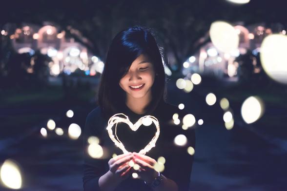 A woman with dark hair standing in a dark night holding a firework that is shaped like a heart.