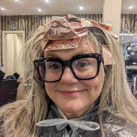 A woman sat in a hairdressers with her hair covered in copper foils for colouring