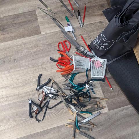 A jumble of jewellery tools on a wooden floor, next to the fallen containers which were meant to be keeping them tidy!
