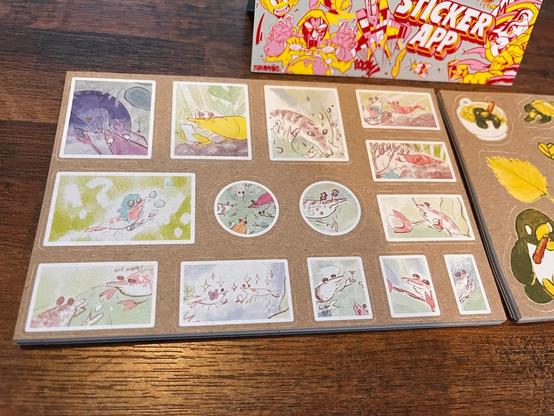 photo of a small postcard-sized stack of sticker sheets printed on kraft paper. there are 14 stickers in total, of various expressive shrimp illustrations contained within white-bordered shapes. 12 designs are rectangular and 2 designs are circular.