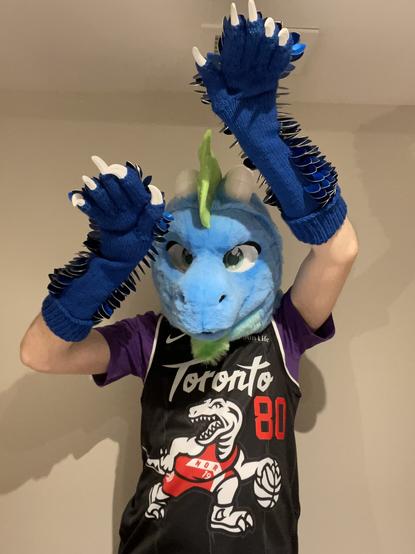 Me in my blue dragon fursuit head and clawed scale gauntlets doing a free throw pose, wearing the new Toronto Raptors city jersey over a purple t-shirt.
It’s a classic 90s style in black, dark grey stripes, white striping, wordmark and raptor, and red jersey number. The raptor is wearing the red Toronto ‘North’ jersey and numbered 19, a reference to their 2019 championship.