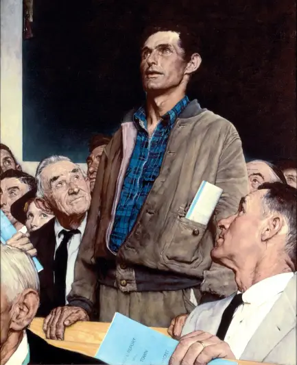 A man stands in a crowd that's sitting and he looks defiant but also matter of fact. The sitting figures are looking at him, listening to what he has to say