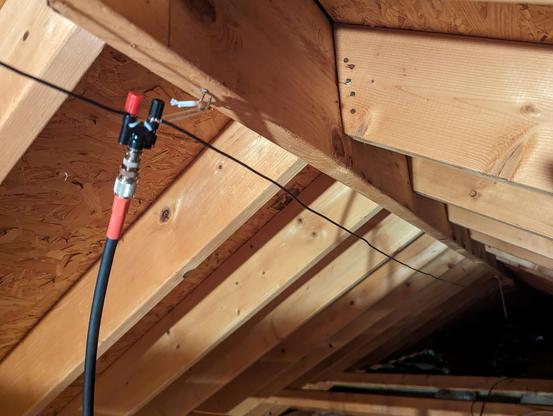 Center of a dipole antenna with a coax cable attached. The antenna is running along the framing under the peak of a roof in an attic.
