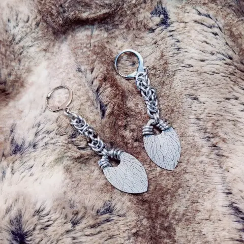 Boucles d'oreilles en maille byzantine, composées d'anneaux en aluminium légèrement brossé qui leur donne un aspect plus blanc, et au bout de chaque chaînette est attachée une écaille au motif de plumes blanches.