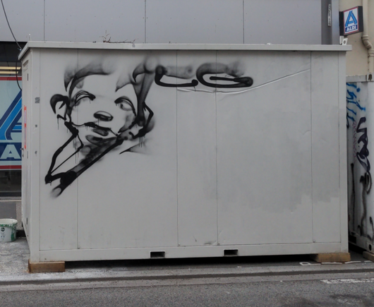 Sur un conteneur blanc posé dans la rue, un visage rond d'enfant a été dessiné à la bombe noire, visiblement à main levée, signé "LG".