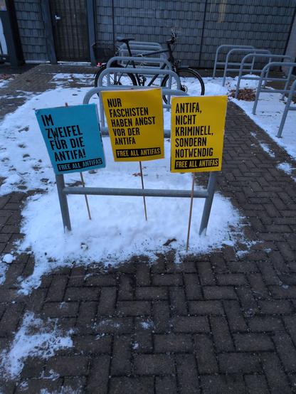Drei Schilder, die an einem Geländer auf von etwas Schnee bedecktem Pflastersteinboden Stehen.

Auf den Schildern stehen Sätze: "Im Zweifel für die Antifa"
'Nur Faschisten haben Angst vor der Antifa' und 'Antifa nicht kriminell sondern notwendig'