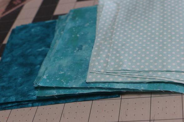 A selection of turquoise square fabrics in piles.  The dark turquiose is on the left, medium value turquoise is in the middle. On the right is pale turquioise with white spots.  I like these colours. Reminds me to tropical islands and snorkelling in the sun.