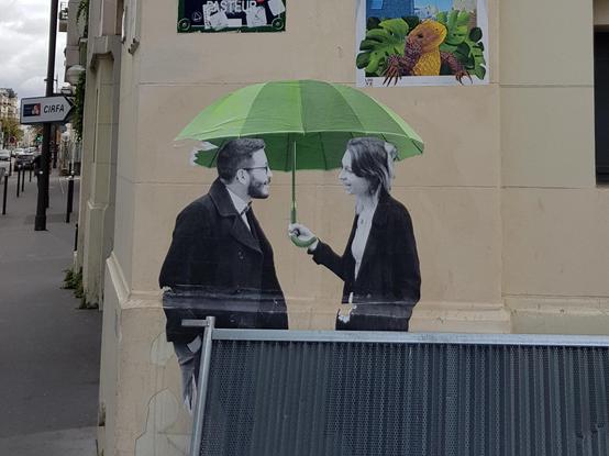 A full size collage of a black & white man and woman talking under a green umbrella on the corner of a building.