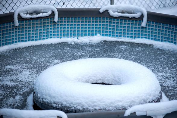 Das Bild zeigt einen zugefrorenen runden Swimmingpool mit einem großen Schwimmreifen welcher mit Pulverschnee bestäubt ist.