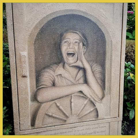 On an electrical box is a painting in light brown tones of a woman shouting something loudly. A passing shower has left a nice pattern of raindrops on the paining.