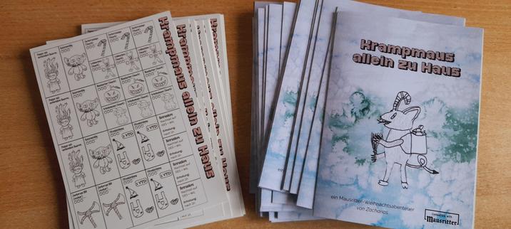 Ein Foto von 2 Stapeln auf einem Holztisch. Ein Stapel besteht aus Gegebständeblättern und der 2. Stapel aus Abenteuerflyer mit dem Titel: Krampmaus allein zu Haus