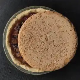 Se démarquant sur le fond d'une table noire, le dos d'un pain rond roussi masque partiellement le disque d'une tarte aux prunes. Dans le croissant qui reste apparent, les prunes cuites constituent un fond coloré sombre oscillant entre orangé et violacé. Le disque de la tarte est serti du beige clair du fond de tarte, puis du verre transparent du plat en Pyrex.