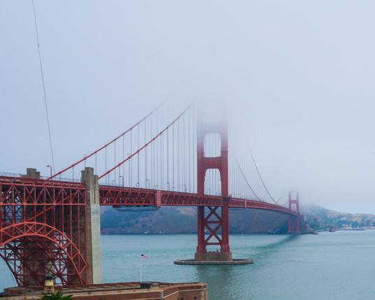 A vibrant red Golden Gate bridge from the San Francisco side (South end) the two suspension towers of the bridge disappear into thick fog.