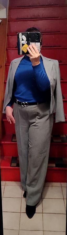 Blue sweater with gold buttons on the shoulder. Light grey wide-leg knit trousers. Black suede ankle boots, black belt with silver circle hardware. Pale grey blazer.