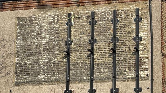 Portion of brick wall exposed by the removal of a billboard which was mounted with vertical beams that are still in place on the wall. Versus the stuccoed portions of wall around the reveal portion, there are fading painted letters in black on the brick section.