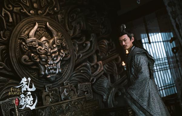 Nie Mingjue stands in profile, head turned in the direction of the viewer, before a wall dominated by layers of massive ornate carvings, the centerpiece of which is a horned head with a mouth full of fangs.
